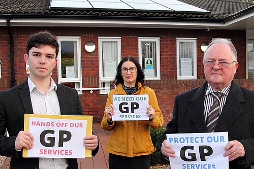 Alex Wagner, Mary Davies & Bernie Bentick outside GP Surgery holding Hands off GP Services